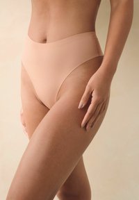 Sous-vêtements beiges taille haute avec un design lisse et sans coutures et une couverture modérée, présentés sur un fond neutre.