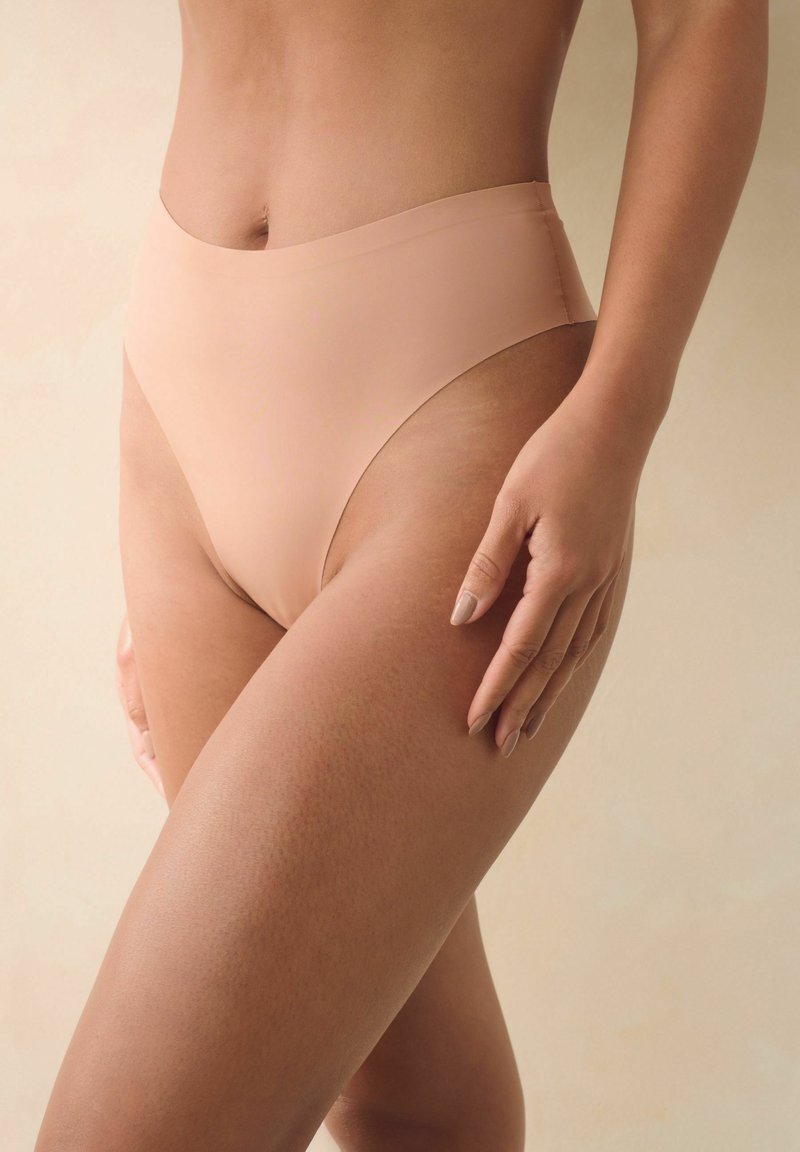 Sous-vêtements beiges taille haute avec un design lisse et sans coutures et une couverture modérée, présentés sur un fond neutre.
