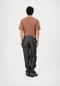 Mørke denim cargo bukser med flere lommer, hvite sømmer og en brun merkelapp. Accompagnert av en brun t-skjorte med korte ermer.