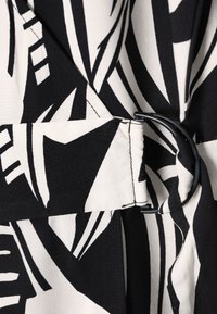 Tissu à motifs noir et blanc présentant des dessins angulaires audacieux ; comprend une ceinture en tissu avec une boucle circulaire noire.