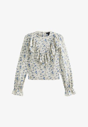 Blusa floral de tela crema, con patrones de flores azules. Detalle frontal con volantes y mangas largas con puños fruncidos. Abertura en la parte posterior con forma de ojo de cerradura.