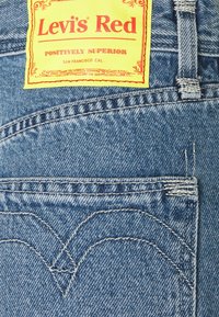 Levi's röda denimmaterial har en gul tagg med röd text, bakfickan har en distinkt sömnad och en blå texturerad finish.