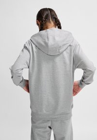 Grauer Kapuzensweater mit langen Ärmeln, aus weichem Material, mit lockerer Passform und gerippten Manschetten. Die Rückansicht zeigt ein schlichtes Design.