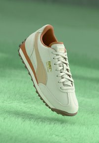 Baskets en textile blanc avec des accents marron clair, présentant une surface texturée, des lacets ronds, un col rembourré et une semelle en caoutchouc avec de petits clous.