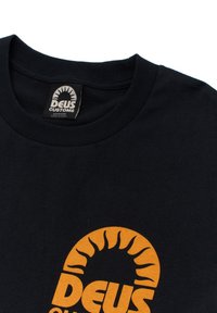 Black cotton t-shirt featuring an orange sun logo with the text "DEUS CUSTOMS." Ribbed crew neckline. Tag displays size medium.