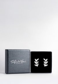 Silverfärgade bladformade örhängen som visas i en svart sammetsträdd, strukturerad mörk låda med en silverlogotyp. Lådan är stängd från vänster.