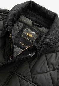 Black quilted jacket interior with corduroy collar, gold zipper, and label stating "Premium Grade, Durable Goods, Regular Fit."