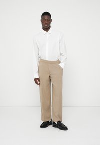 Weißes Langarmhemd mit spitzem Kragen, kombiniert mit beigen, weit geschnittenen Hosen und schwarzen Schuhen, mit einem lässigen Schnitt und subtiler Textur.