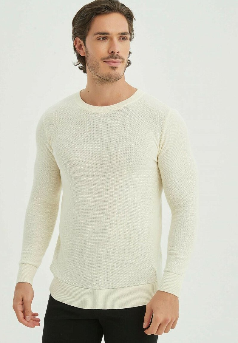 Pull crème à manches longues avec un tissage texturé, col rond et bords-côtes aux poignets et à l'ourlet, porté avec un pantalon noir.