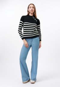 Black and white striped knit sweater with a mock neck, featuring three buttons on the shoulder, paired with light blue flared jeans.