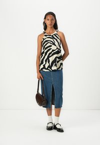 Top leggero senza maniche con strisce zebra nere e crema, abbinato a una gonna di jeans con spacco frontale e mocassini neri. Borsa a spalla marrone.