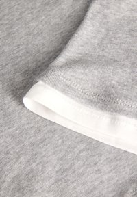 Grey cotton fabric with a smooth texture; features a white cuff and stitching details along the hem. Close-up view of shirt material.