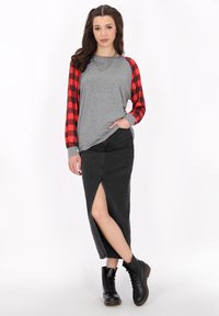 Grå långärmad skjorta med rödrutiga ärmar, ihop med en svart denimkjol med en slits fram och svarta snörboots.