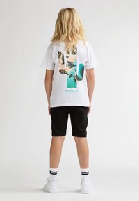 Camiseta blanca con un gráfico colorido de un cactus y una escena de playa en la parte trasera. Combina con pantalones cortos negros y zapatillas blancas.