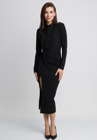 Czarna sukienka midi z długimi rękawami, z wykrzywionym przodem i szczeliną z przodu. Miękka tkanina o gładkiej strukturze. Klasyczna sylwetka.