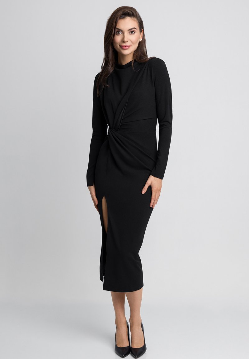 Czarna sukienka midi z długimi rękawami, z wykrzywionym przodem i szczeliną z przodu. Miękka tkanina o gładkiej strukturze. Klasyczna sylwetka.