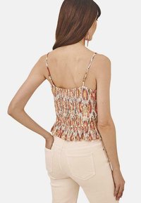 Top peplum de tirantes finos, con un diseño abstracto mezclado en tonos de naranja, rosa y crema. Detalle de tela texturizada.