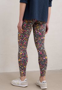 Zwarte leggings met bloemmotief en meerkleurige fruit- en bladdesigns; rekbare stof; gecombineerd met witte sneakers.
