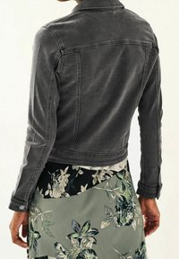 Gray denim jacket with a fitted design, buttoned cuffs, and pronounced seams, worn over a floral-patterned skirt.