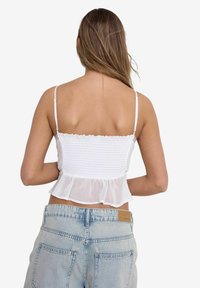 White smocked crop top with thin straps and a ruffled hem, paired with high-waisted light blue denim jeans.