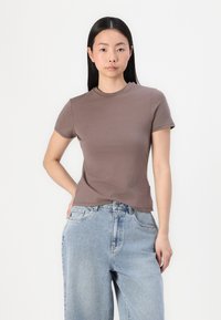 Kortsleeve, rundhalset brun topp laget av glatt stoff, sammen med lyseblå, løstsittende denimjeans. Enkel design, ingen synlige mønstre.