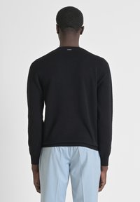 Maglione nero con texture, colletto rotondo e maniche lunghe, abbinato a pantaloni blu chiaro. Design semplice, senza motivi o dettagli visibili.