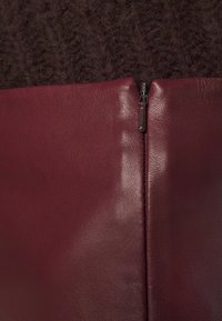 Bordeauxrotes Lederpaneel mit einem strukturierten, flauschigen dunkelvioletten Material über einem Reißverschluss, das den Kontrast zwischen glatter und rauer Oberfläche zeigt.