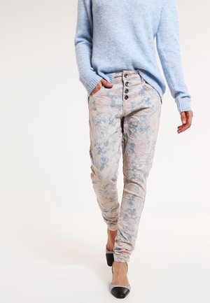 Un pull bleu clair associé à un pantalon ajusté à motifs floraux dans des teintes claires, avec un détail de cinq boutons et des poches ; des chaussures à talons noires et blanches.