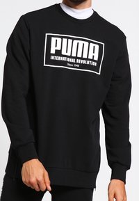 Felpa nera in misto cotone, con un grande logo bianco che recita "PUMA INTERNATIONAL REVOLUTION" e polsini e orlo a coste.