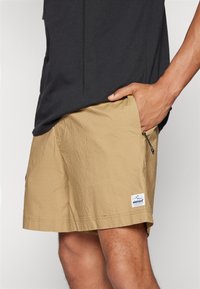 Khaki shorts lavet af letvægtsstof, med en sidelomme med lynlås, en struktureret overflade og et lille mærke på kanten.