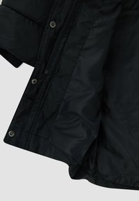 Chaqueta acolchada negra con cierre de cremallera, botones a presión y una textura suave y lisa. Incluye un detalle de puño en contraste negro.