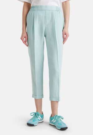 Woman wearing light blue cropped trousers with cuffed hems and matching light blue sneakers, standing against a plain background.