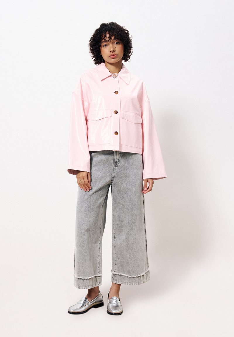 Rosa, glänzende, kurz geschnittene Jacke mit zwei vorderen Taschen und Knopfverschluss, kombiniert mit weit geschnittenen, ausgefransten grauen Denim-Hosen und silbernen Slippern.