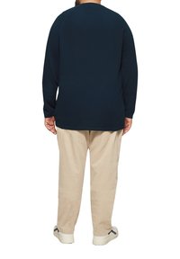 Marineblaues Langarmshirt mit Rundhalsausschnitt, kombiniert mit beigen Cordhosen. Das Outfit zeichnet sich durch eine lockere Passform und bequeme Materialien aus.