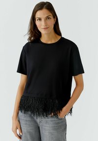 Schwarzes Kurzarmoberteil mit einem verkürzten Design und einem fransigen Saum. Der Stoff ist glatt, und die Fransen verleihen Textur und Details.