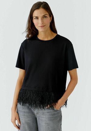 Black short-sleeved top featuring a cropped design with a fringed hem. The fabric is smooth, and the fringe adds texture and detail.