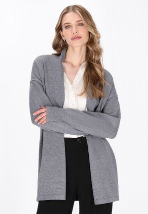 Cardigan grigio a maglia con maniche lunghe, vestibilità morbida, aperto davanti e polsini a costine, indossato sopra una blusa in satin chiaro e pantaloni neri.