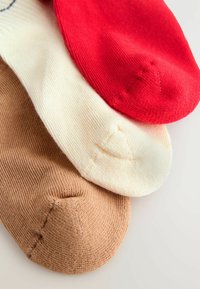 Tre paia di calzini: un paio rosso, un paio crema e un paio marrone. Tutti sono lavorati a maglia, con trame testurizzate visibili e punte arrotondate.