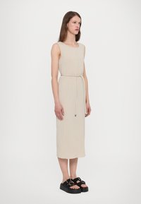Rochie midi ribbed bej, cu decolteu rotund și talie legată, asortată cu sandale pe platformă cu catarame duble.