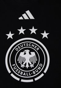 T-shirt preta com um logotipo redondo branco que apresenta uma águia, cinco estrelas acima e "DEUTSCHER FUSSBALL-BUND" em texto negrito. Logotipo da Adidas em branco.