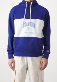 Niebieska i biała bluza z kapturem z zamkiem na ćwierć. Na piersi znajduje się napis "Champion Rochester 1919" w jasnoniebieskim kolorze oraz logo na rękawie.