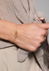 Złota bransoletka łańcuszkowa z dwoma geometrycznymi kształtami: heksagonem i oktagonem. Delikatny design o gładkim wykończeniu, noszona na dłoni.