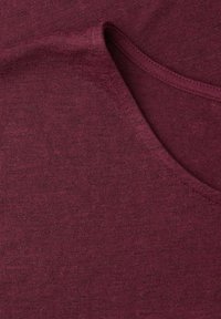 Gros plan sur un tissu tricoté bordeaux plié montrant la texture et les coutures détaillées le long d'une couture courbe.