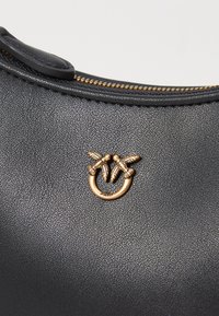 Melnā teksturētā ādas soma ar zelta tonī akcentiem ar savītu dizainu, kurā ir redzama ripa gar augšējo malu.