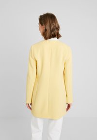 Gelbes tailliertes Blazer mit Reverskragen, langen Ärmeln und strukturiertem Schnitt. Glatte Textur mit einem Schlitz hinten.