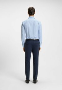 Camicia azzurro chiaro con maniche lunghe, abbinata a pantaloni blu scuro, con una cintura nera e scarpe nere lucide.