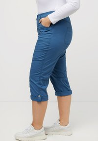 Pantalons courts bleus en tissu léger, dotés de poches latérales et de manches retroussées. Portés avec des baskets blanches.