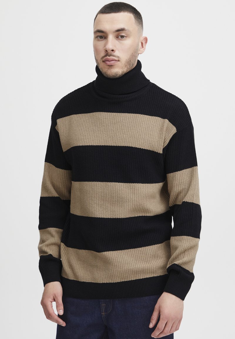Svart og beige stripete genser med høy hals, ribbet tekstur og lange ermer, med brede horisontale striper.