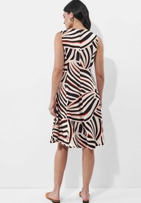 Ärmelloses Kleid mit ausgestelltem Schnitt und kräftigen, wellenförmigen Mustern in Schwarz, Weiß und Rot. Hergestellt aus einem glatten, leichten Stoff.