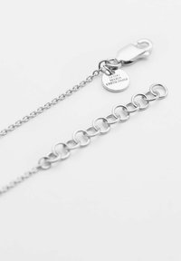 Bracciale in metallo argentato con chiusura a moschettone e ciondolo circolare. Presenta un design a catena collegata con maglie alternative lisce e ovali.